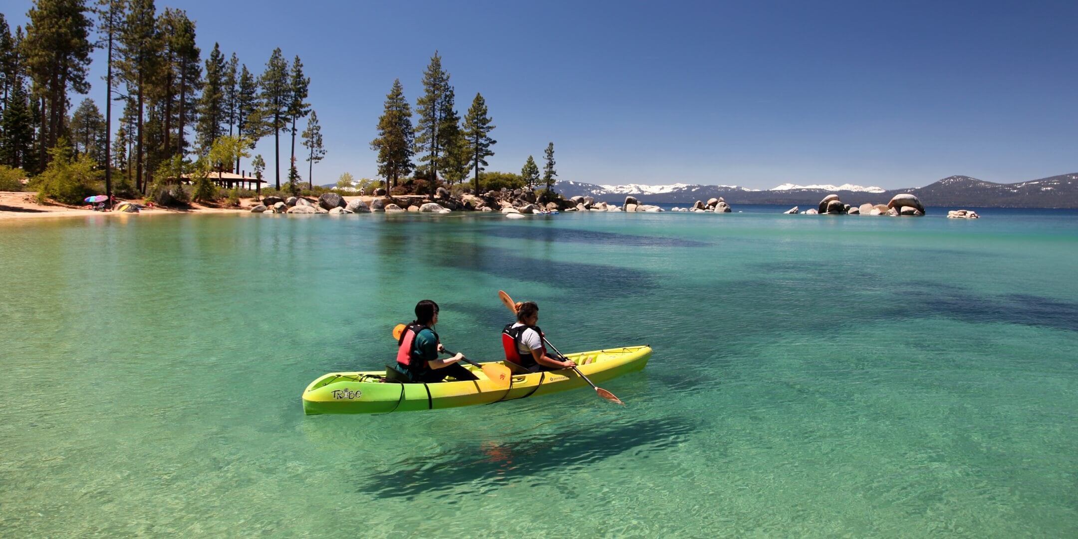 Two people wear lifejackets as they kayak on in Sand Harbor at Lake Tahoe