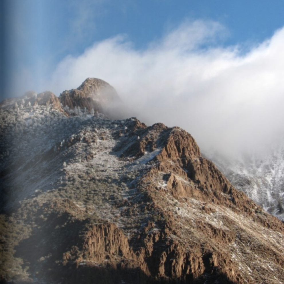 Snow-dusted mountain top with clouds moving over it.